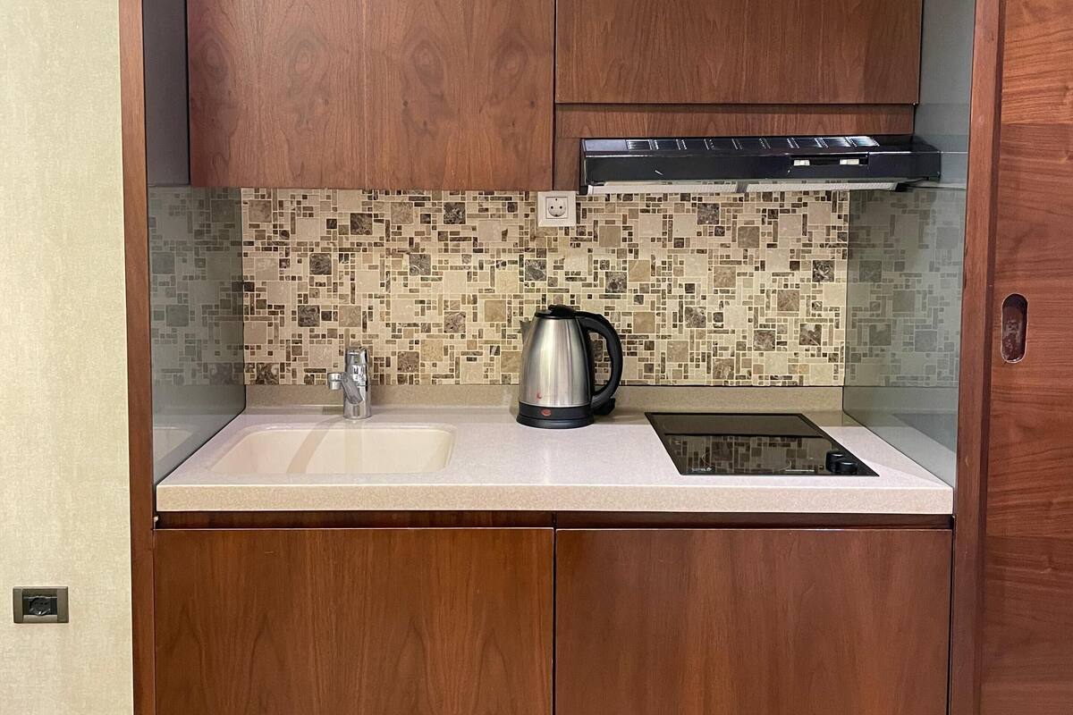 A compact kitchen with wooden cabinets, a tiled backsplash, and a stainless steel kettle.