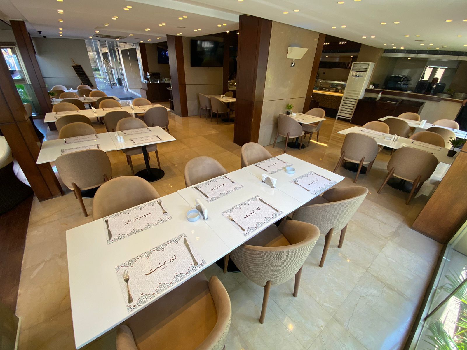A restaurant with multiple tables set for dining, featuring a modern interior with a mix of natural and artificial lighting.