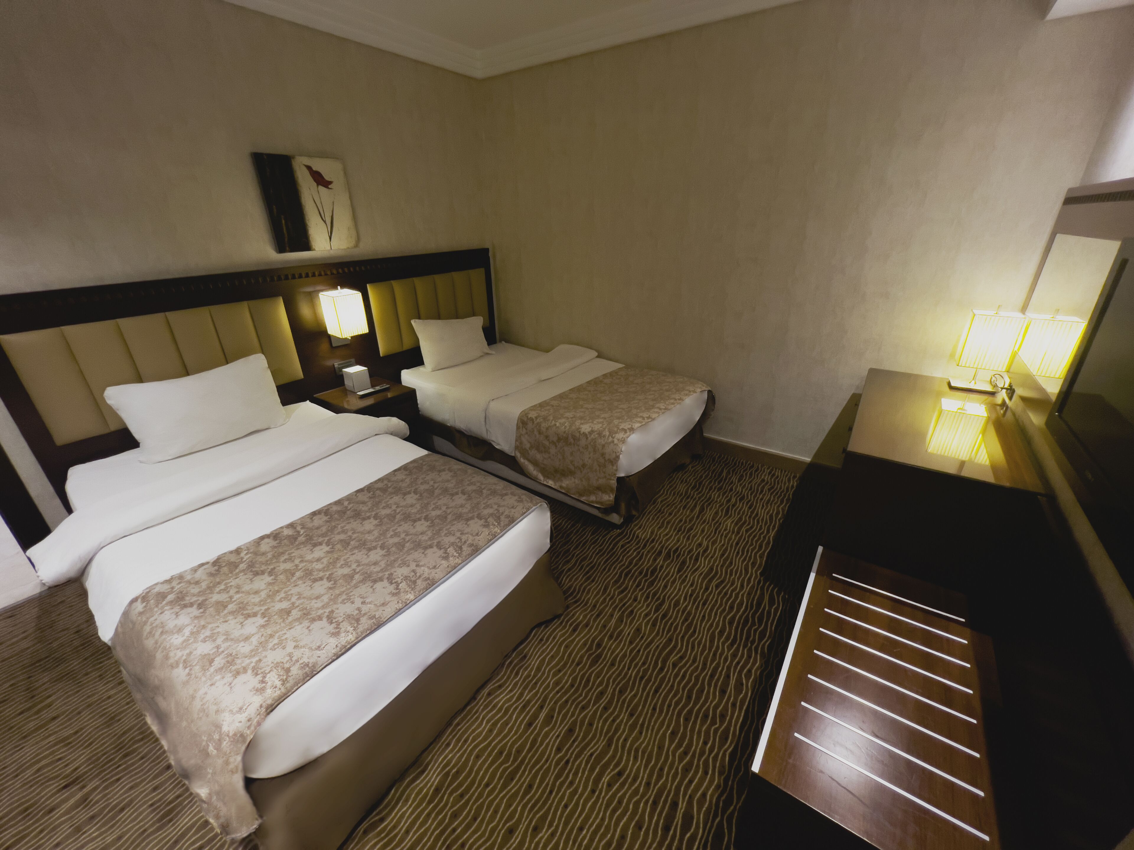 Une chambre d’hôtel avec deux lits, une table de chevet, une lampe et un bureau en bois avec un miroir.