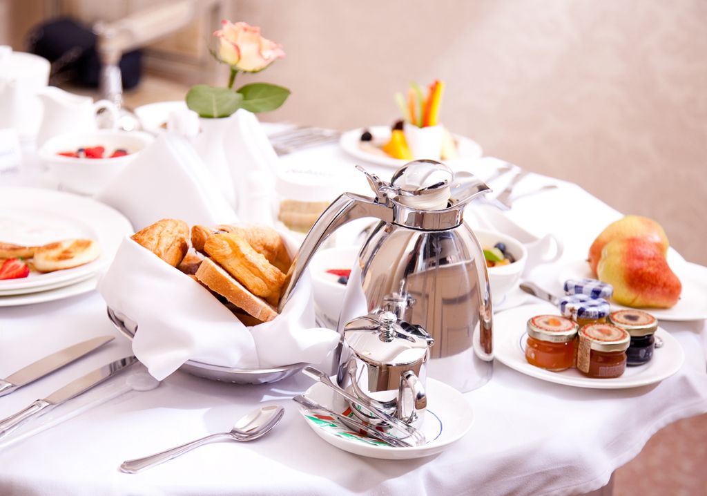 A breakfast setting with croissants, a coffee pot, and jam jars on a table.