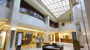 A spacious lobby with a high ceiling, a reception desk, seating areas, and a glass railing overlooking the lower level.