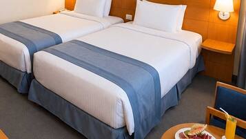 A hotel room with two beds, a small table with a plate of fruit and a drink, and a nightstand with a lamp.
