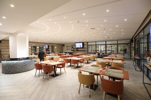 Un restaurante amplio con varias mesas y sillas, una barra central y una pantalla de televisión.