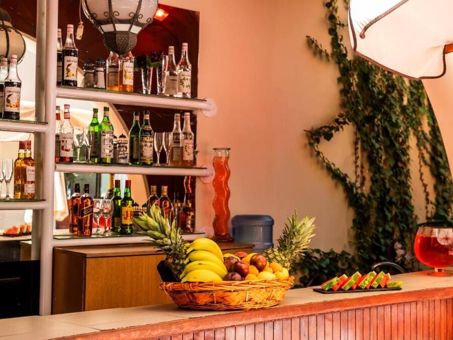 A bar area with shelves of liquor bottles, a fruit basket, and a red cocktail glass.