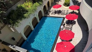 A swimming pool with red umbrellas, lounge chairs, and a tiled deck.