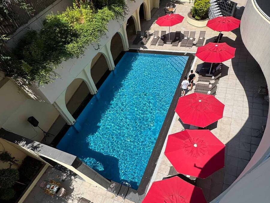 Una piscina con sombrillas rojas, sillas de descanso y un suelo de baldosas.
