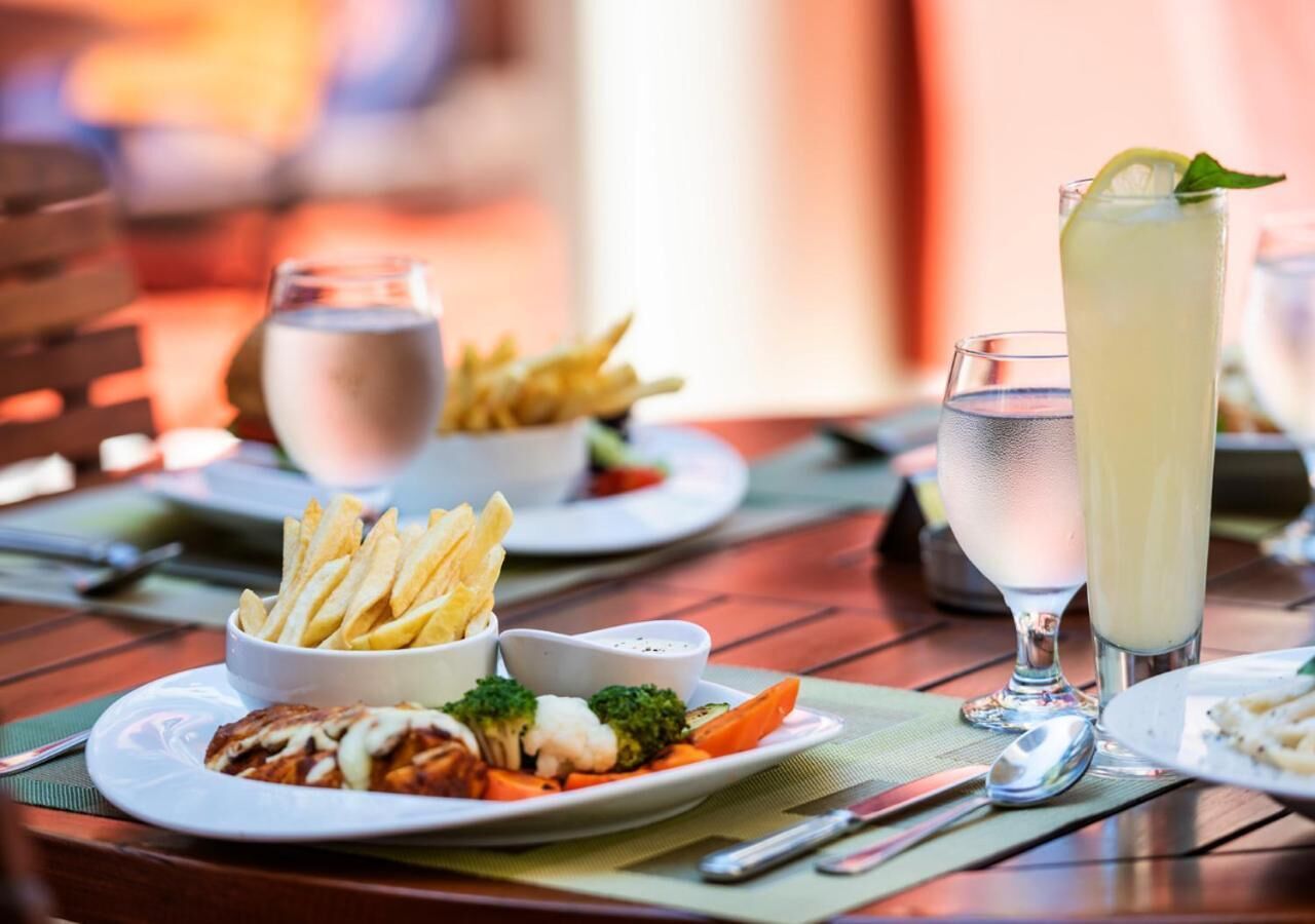A dining table with plates of food, including fries, vegetables, and a creamy dish, along with glasses of water and a tall drink.