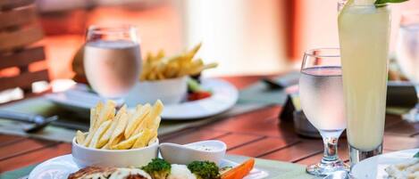 A dining table with plates of food, including fries, vegetables, and a creamy dish, along with glasses of water and a tall drink.