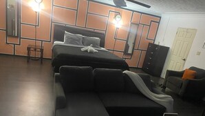 Un dormitorio moderno con una cama grande, un sofá, una mesita y un ventilador de techo.