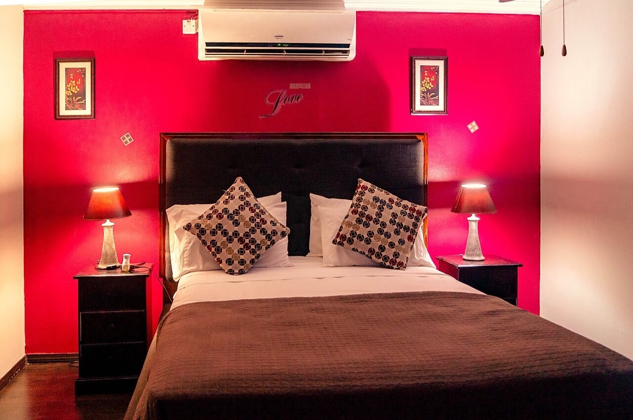 A hotel room with a red wall, a black headboard, and two bedside lamps.