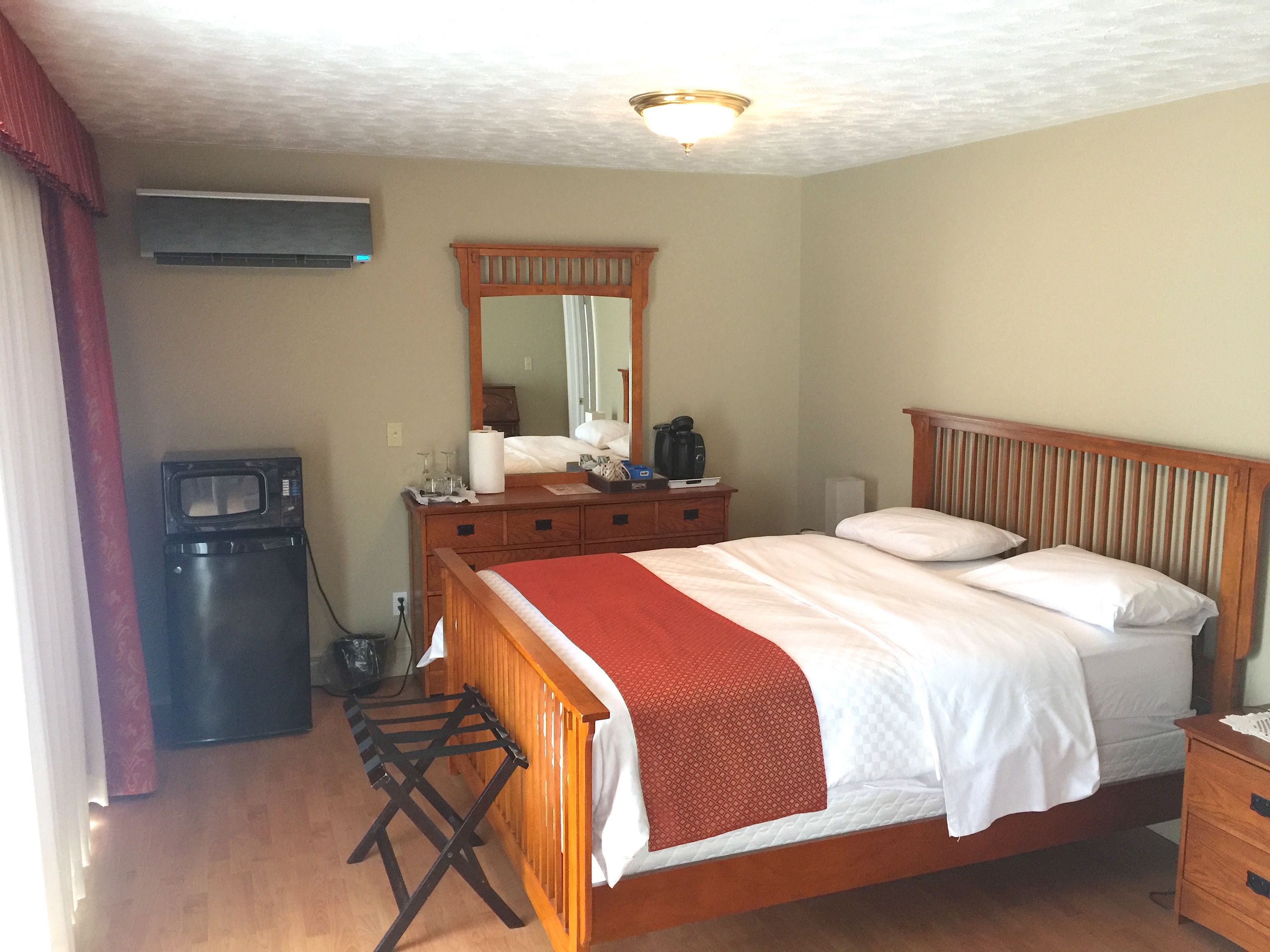 Une chambre avec un lit en bois, une commode, un miroir et un petit coin cuisine.