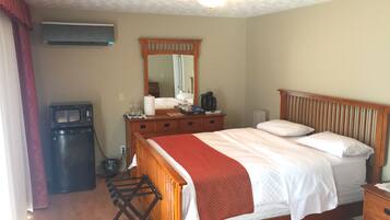 Une chambre avec un lit en bois, une commode, un miroir et un petit coin cuisine.