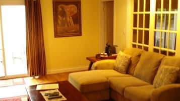 A living room with a beige sofa, a coffee table, a painting of an elephant, and a window with blinds.