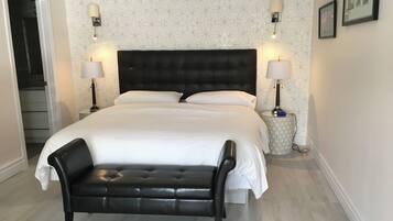A hotel bedroom with a large bed, two bedside lamps, a black leather bench, and a patterned wallpaper.
