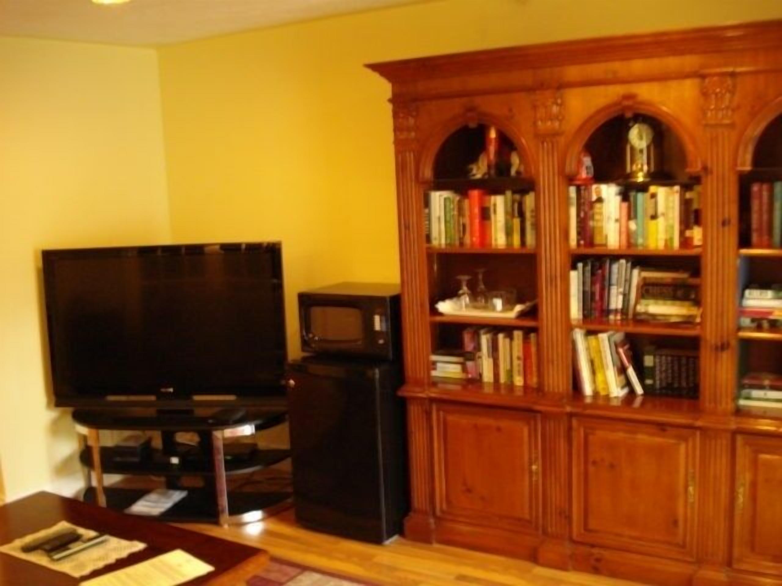 Una sala de estar con televisor de pantalla plana, una estantería de madera y una pequeña mesa con documentos.