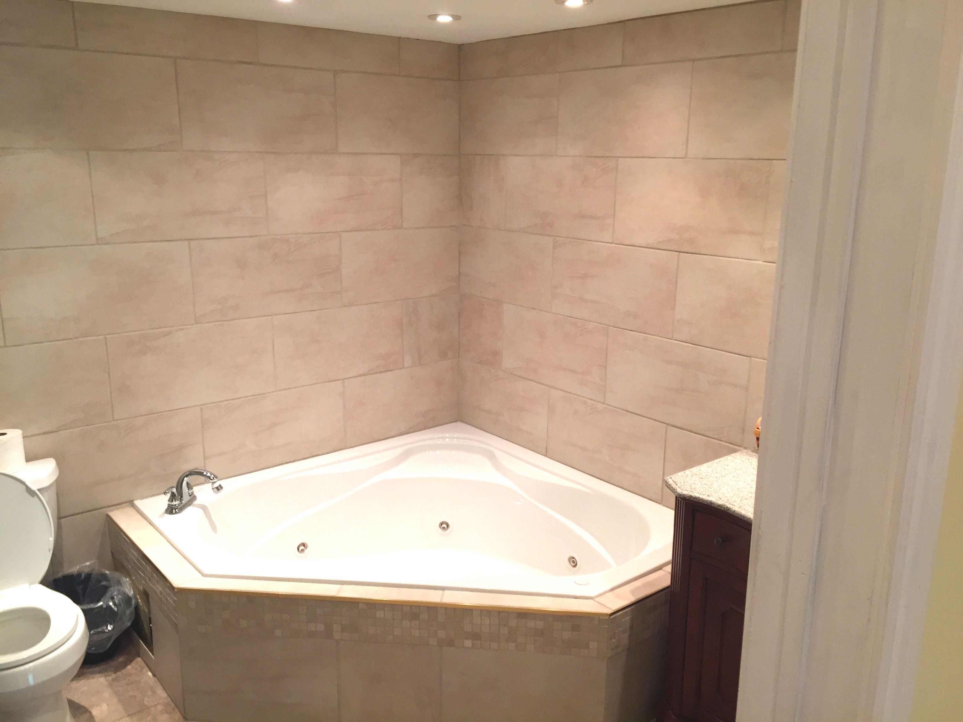 A bathroom with a corner bathtub, a toilet, and a trash bin.