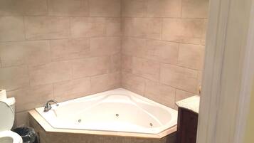 A bathroom with a corner bathtub, a toilet, and a trash bin.