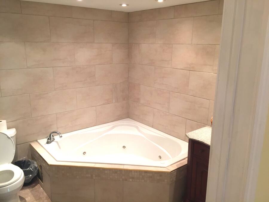 A bathroom with a corner bathtub, a toilet, and a trash bin.