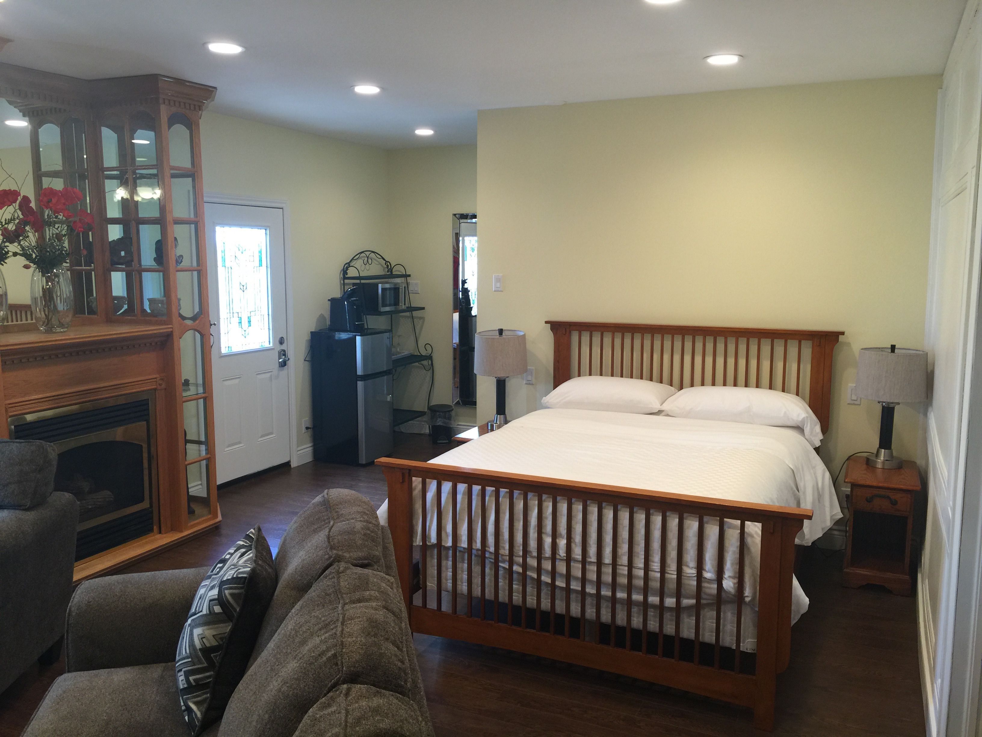 A bedroom with a wooden bed, a fireplace, a dining area with a table and chairs, and a kitchen area with appliances.