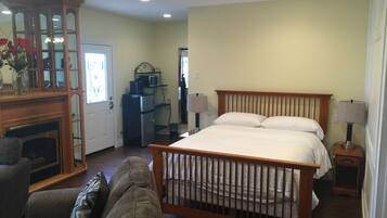 A bedroom with a wooden bed, a fireplace, a dining area with a table and chairs, and a kitchen area with appliances.