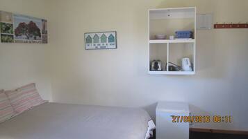 Un dormitorio con una cama, un pequeño armario blanco con estantes y un cuadro colgado en la pared.