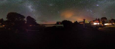A starry night sky with a vehicle and trees in the foreground.