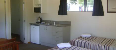A compact room with two single beds, a small kitchenette with a microwave, and a window with curtains.