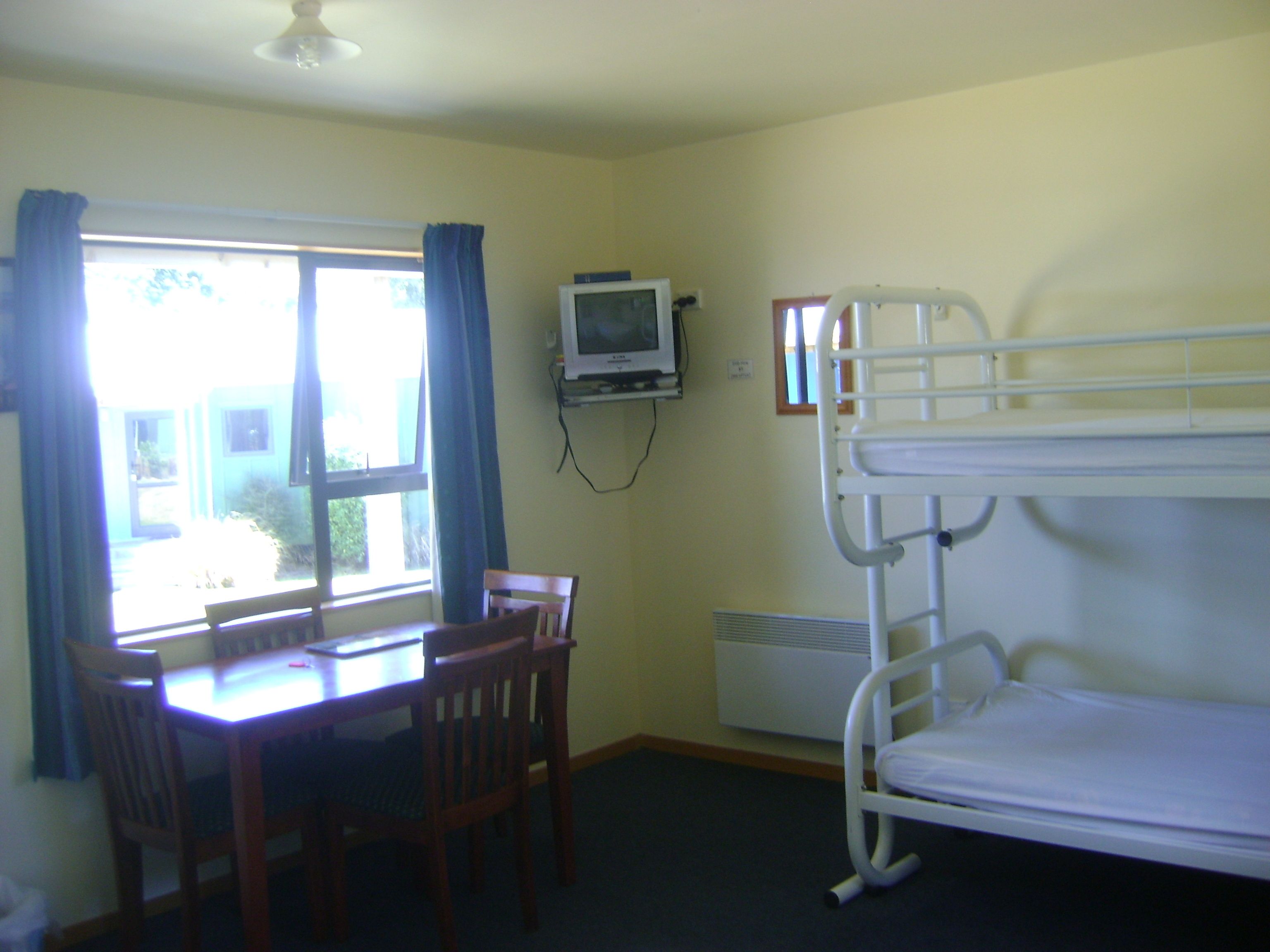 A room with a bunk bed, a desk with a chair, a television, and a window with curtains.