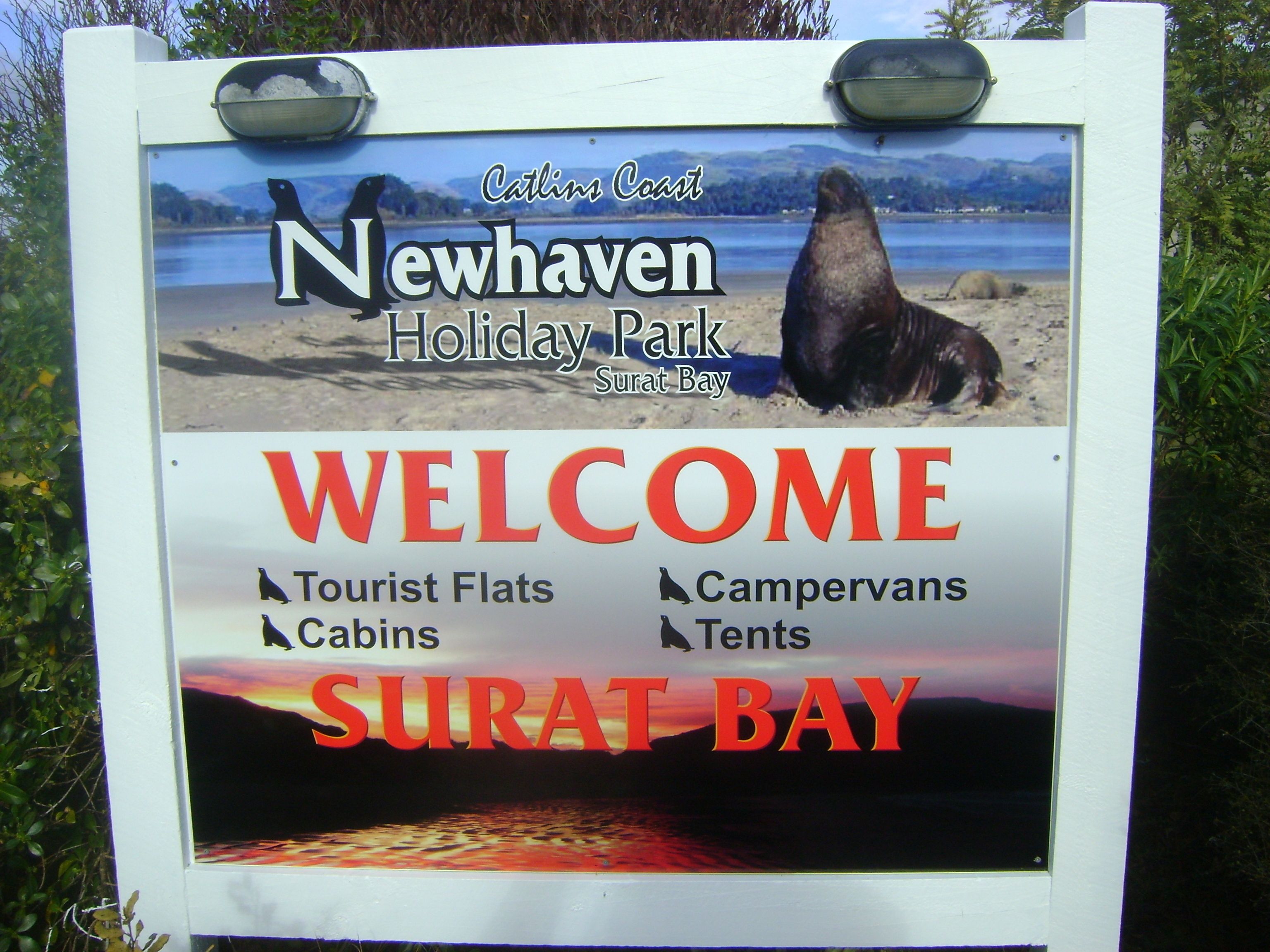 Placa de boas-vindas para o Newhaven Holiday Park em Surat Bay, com apartamentos para turistas, cabanas e tendas.