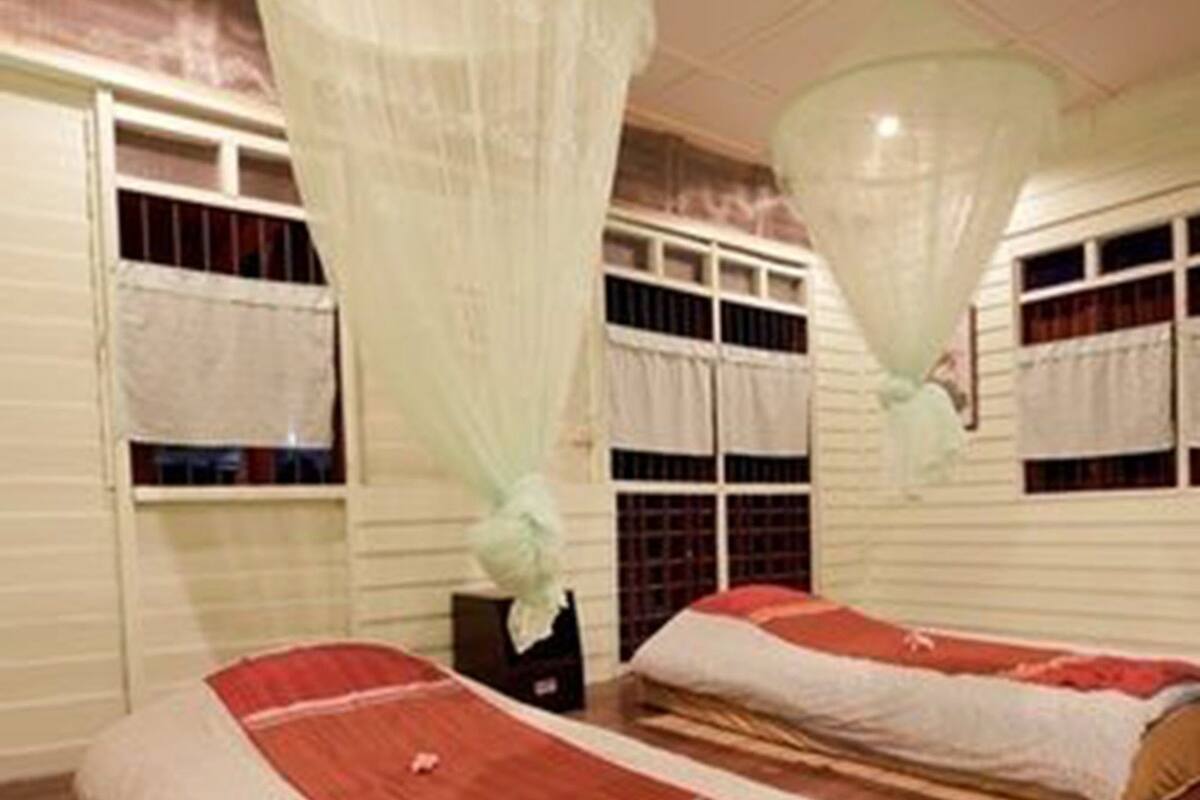 Een kamer met twee bedden, elk voorzien van een klamboe. De kamer heeft houten vloeren en witte muren met ramen.