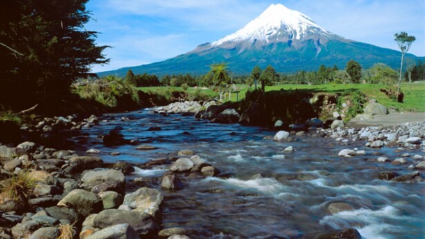 A river flowing through a rocky landscape with a snow-capped mountain in the background.