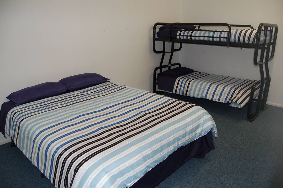 A room with two bunk beds, one with a striped bedspread and pillows, and the other with a striped mattress cover.
