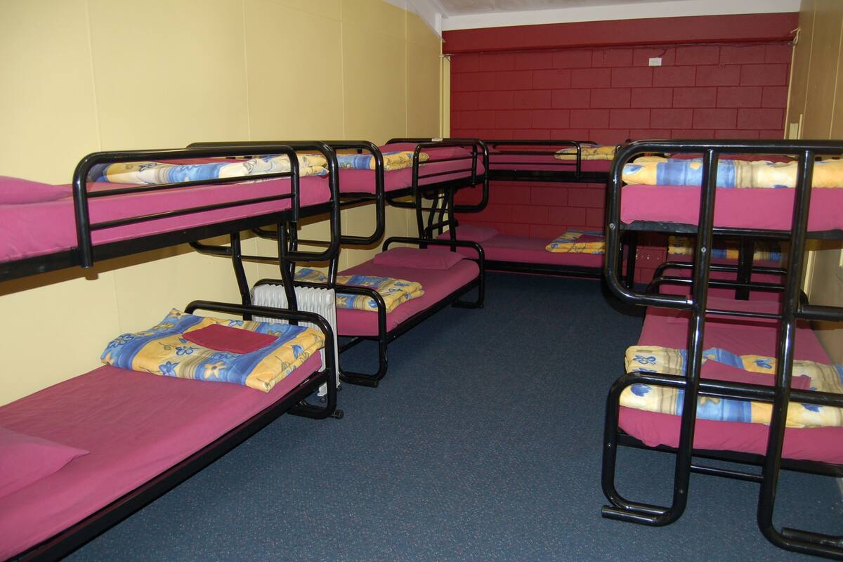 A dormitory room with bunk beds arranged in a corner, each with a pink mattress and blue bedding.