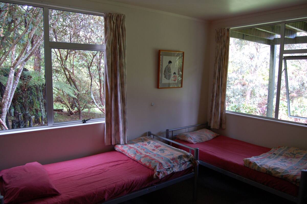 A dormitory room with two beds, large windows, and a framed picture on the wall.