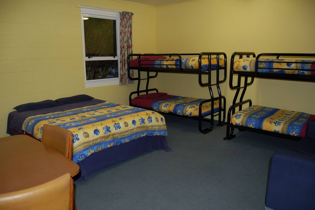 A dormitory room with bunk beds, a single bed, a table, and a window with curtains.