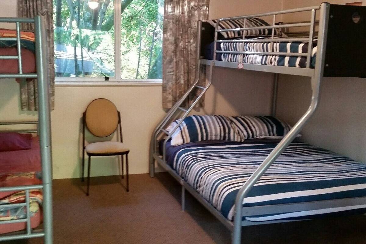 A bunk bed room with a window, a chair, and a bed with striped bedding.