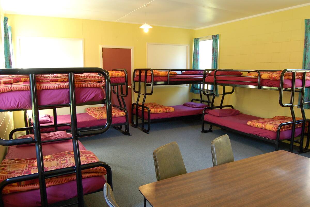 A dormitory room with bunk beds, a wooden table, and chairs.