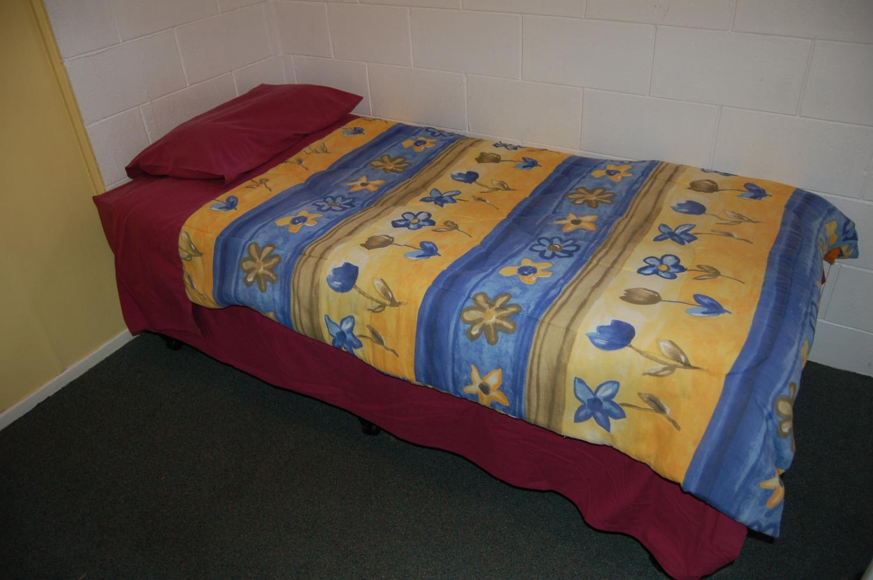 A single bed with a red headboard and a floral-patterned bedspread.