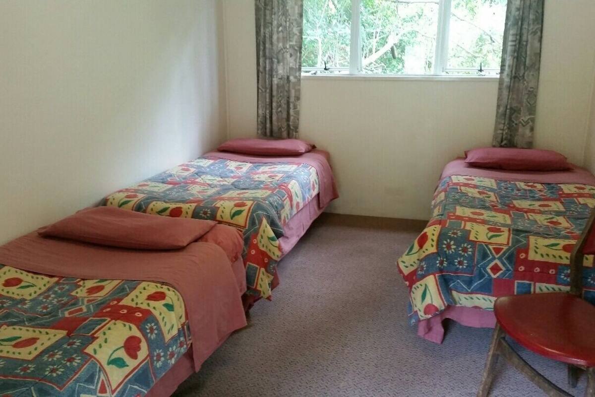 A room with two single beds, each with a colorful patterned bedspread and matching pillows. There is a red chair to the right of the beds.