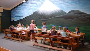 A group of people seated at wooden tables in a room with a mural of a mountain and clouds.