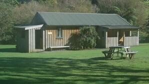 A wooden cabin with a sloped roof, a bench, and a picnic table in front.