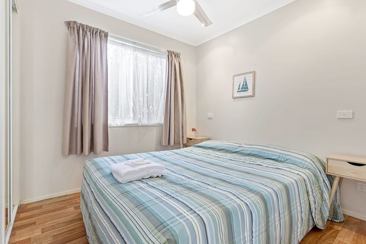 A bedroom with a bed, a window with curtains, a ceiling fan, and a wall-mounted light switch.