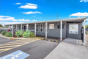 A single-story building with a grey exterior and a covered entrance area. There is a sign indicating the office location. - Lifestyle Villages Redhead (Newcastle)