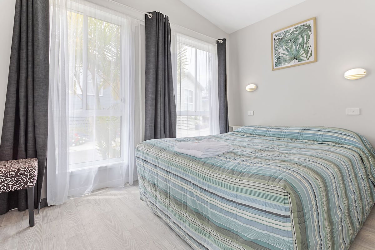 A bedroom with a bed, a bench, and a window with curtains.