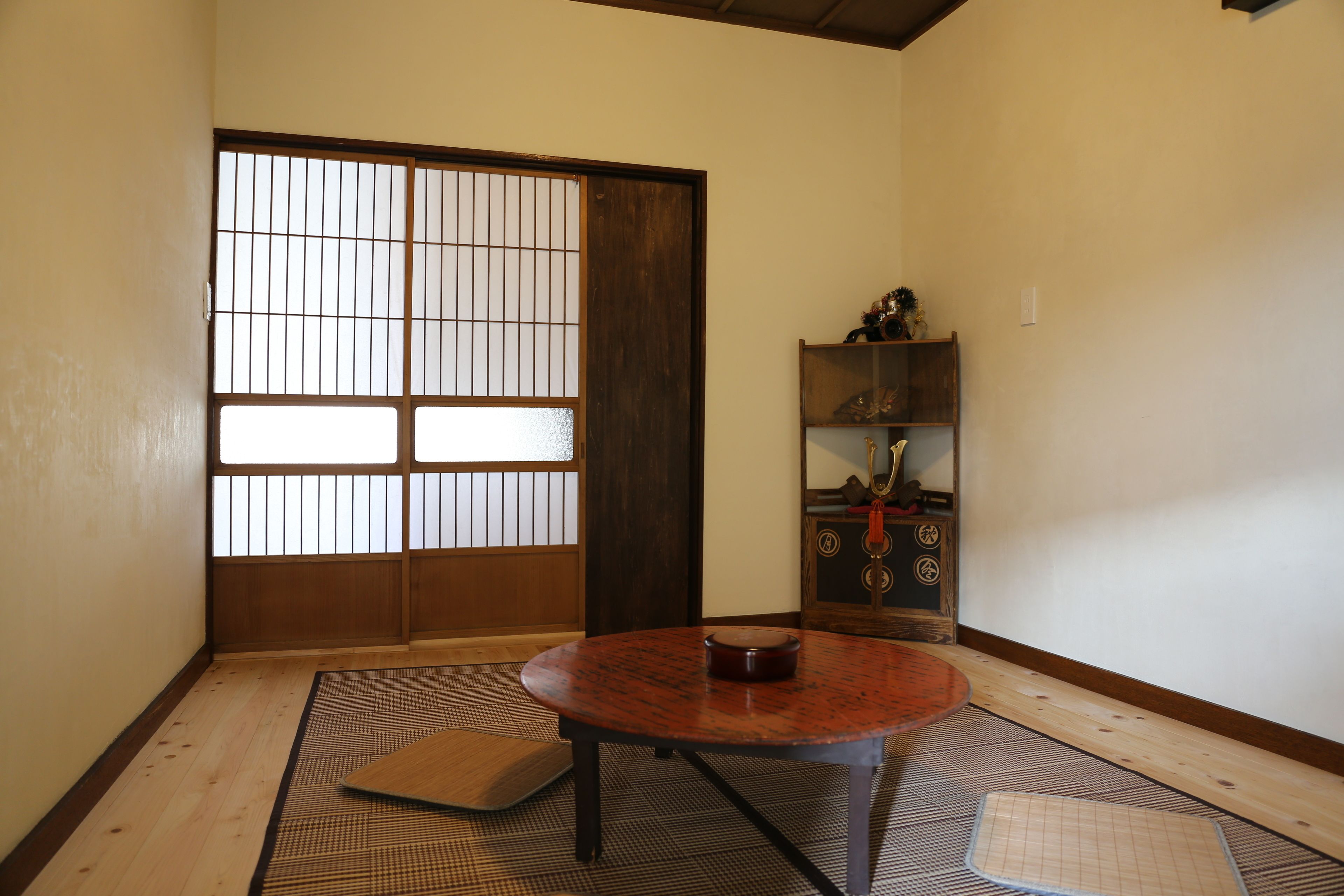 A traditional Japanese room with tatami flooring, a shoji screen door, a wooden table, and a shelf with decorative items.