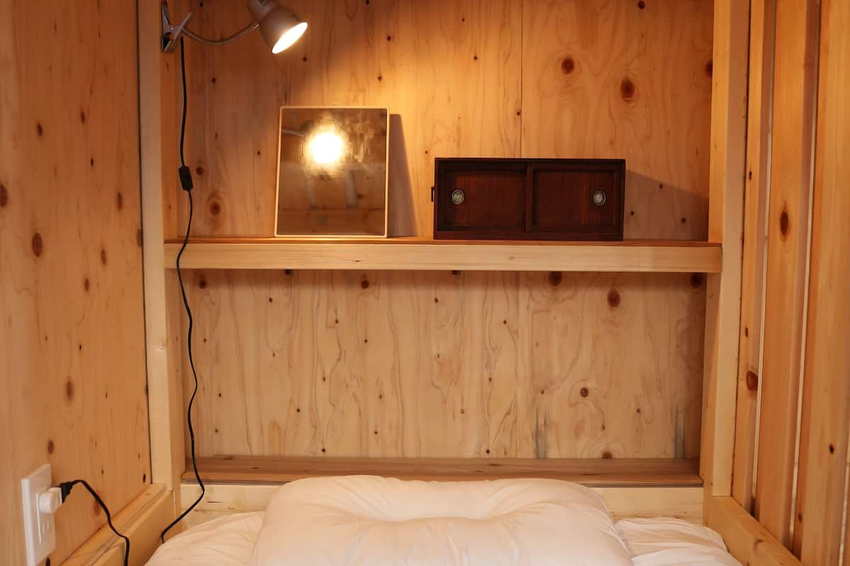 Une pièce aménagée comme un chalet en bois, avec un lit, une étagère sur laquelle se trouve une lampe et une prise électrique.