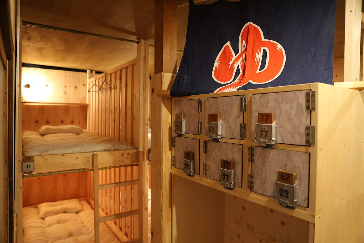 Une chambre avec un lit superposé en bois, composé d’un lit supérieur et d’un lit inférieur. Des compartiments de rangement numérotés se trouvent sous le lit.