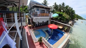 A two-story building with a pool and a red umbrella. - L&M Hearthstones Lodge (Oslob)