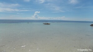 A beach with clear turquoise water and a few boats. - L&M Hearthstones Lodge (Oslob)