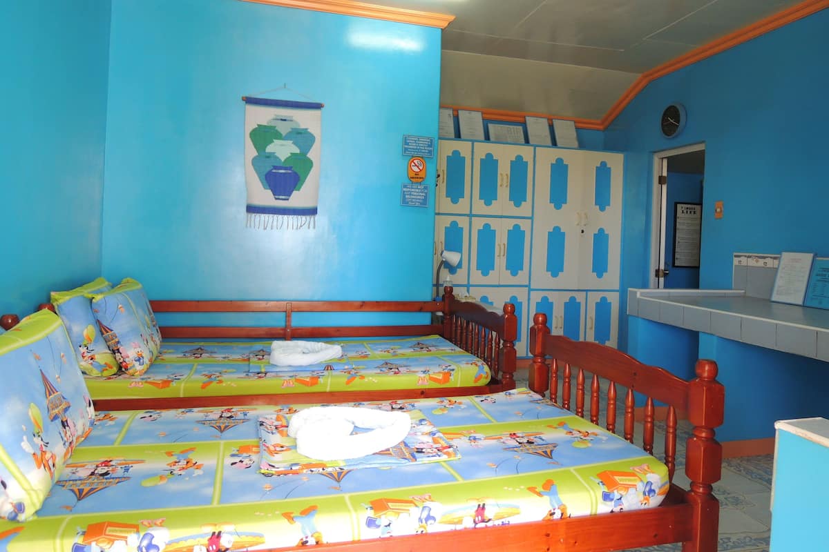Una habitación con paredes azules, una cama con ropa de cama temática de dibujos animados, un cabecero de madera y un escritorio pequeño con un reloj.